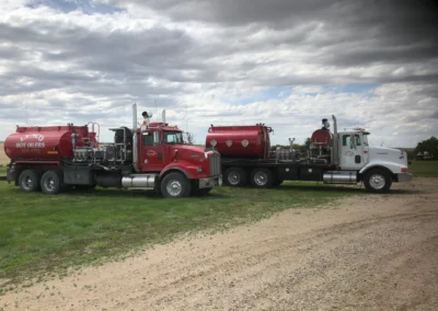 A side view of two tanker trucks parked on a grassy field with a dirt road.